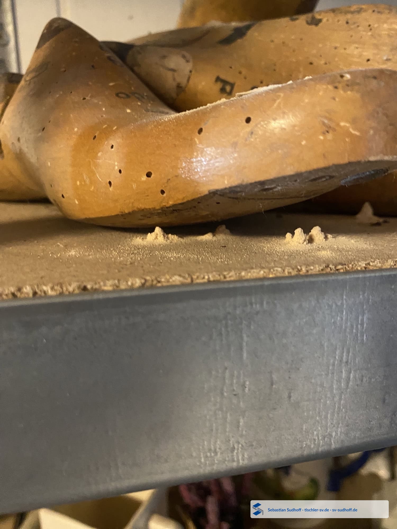 Alte hölzerne Schuhleisten mit zahlreichen Ausflugöffnungen und Bohrmehlhäufchen direkt darunter