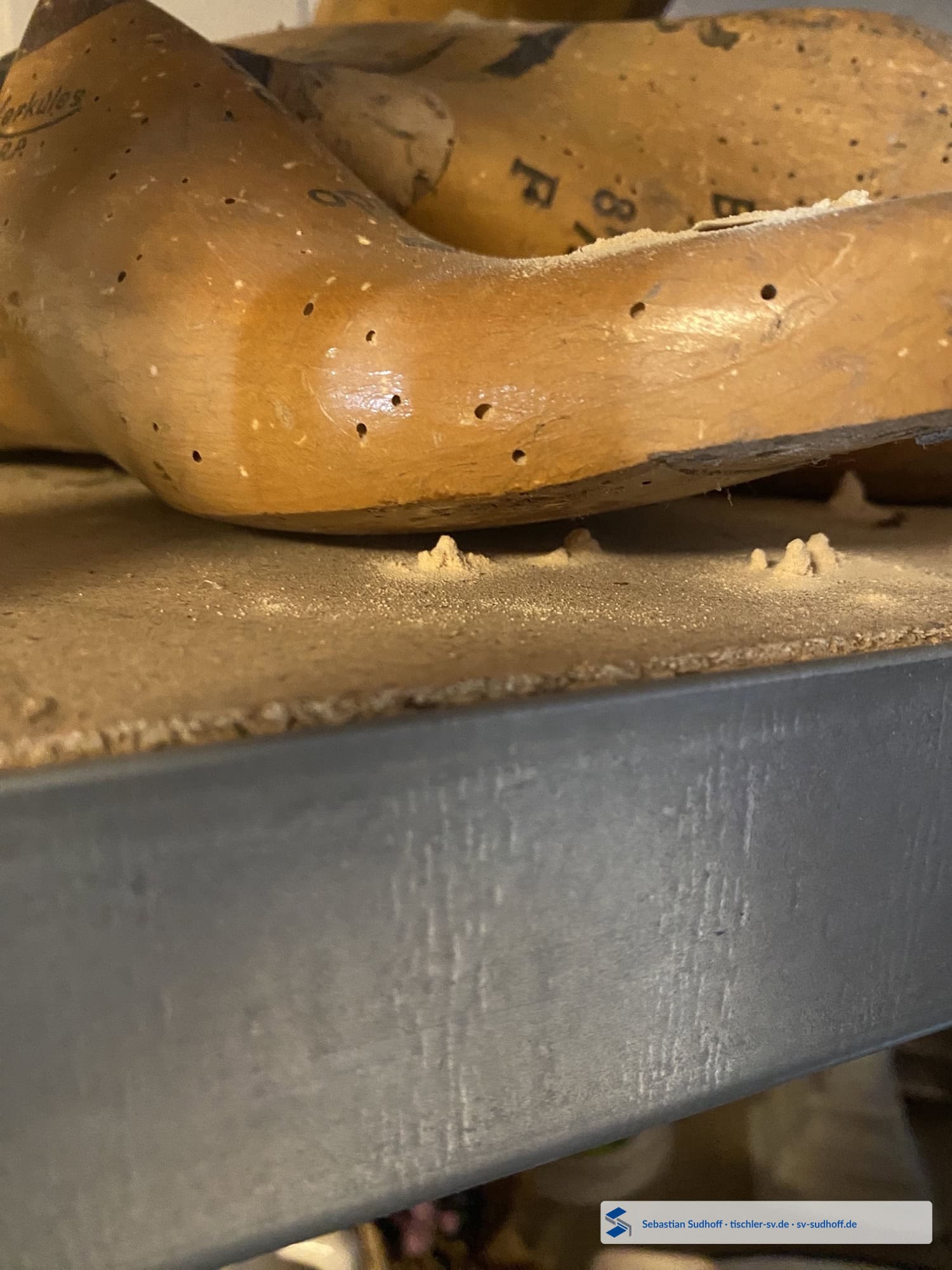 Detailaufnahme von hellem Bohrmehl unter einer alten hölzernen Schuhleiste mit Fraßöffnungen