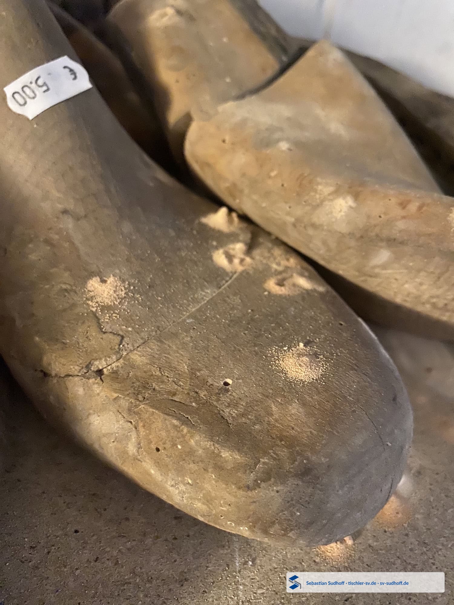 Alte hölzerne Schuhleisten mit rundlichen Ausflugöffnungen und sichtbarem Bohrmehl auf den Holzoberflächen